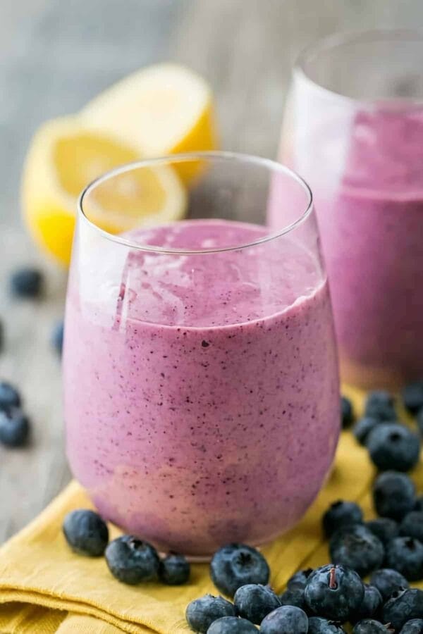 Detox Blueberry Mango smoothie in a glass, on my kitchen counter, surrounded by fresh fruit and vegetables.