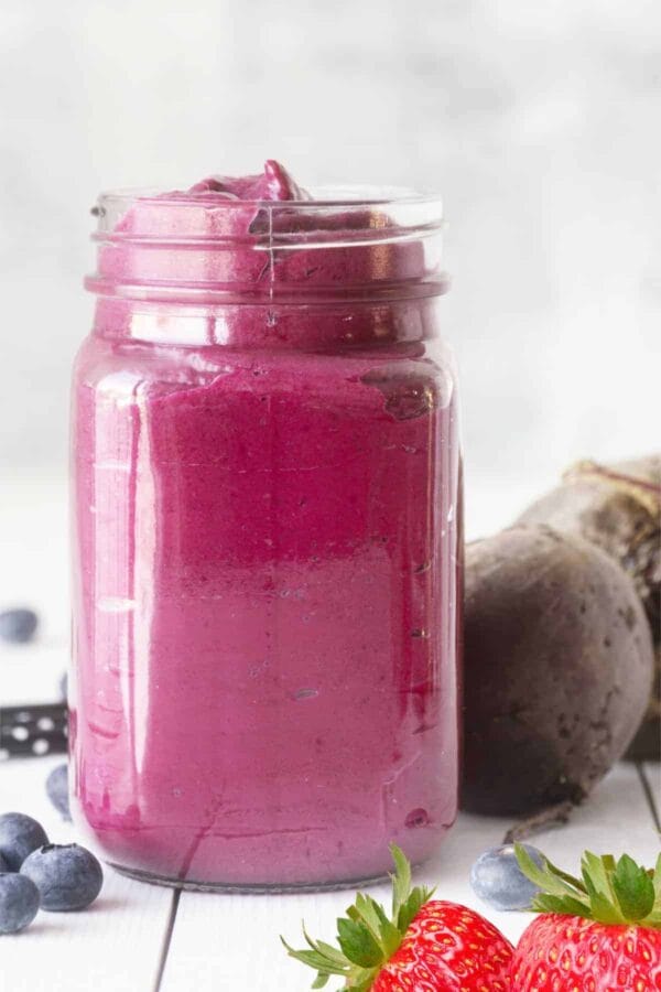 Cholesterol-Lowering Beet Berry smoothie in a glass, on my kitchen counter, surrounded by fresh fruit and vegetables.