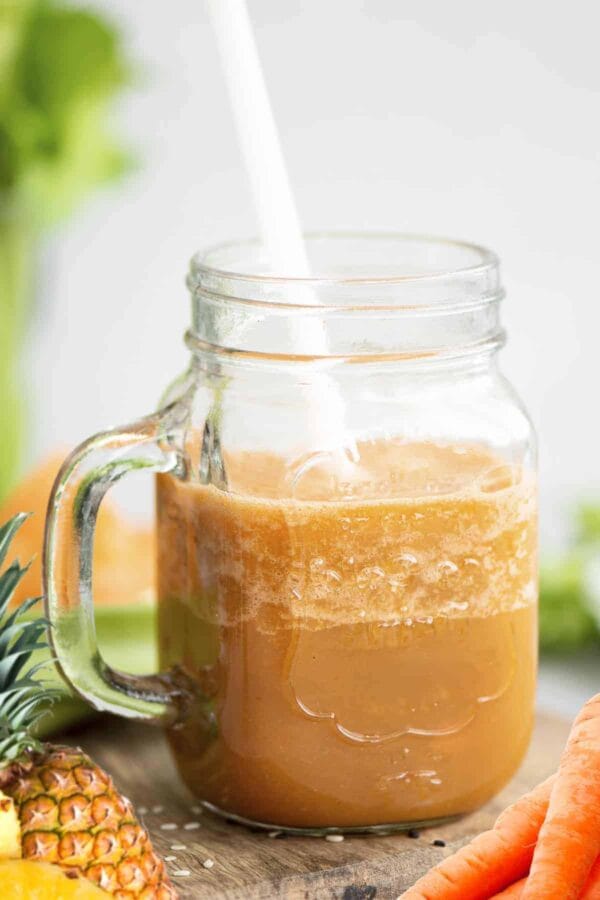 Cholesterol-Lowering Carrot Cake smoothie in a glass, on my kitchen counter, surrounded by fresh fruit and vegetables.