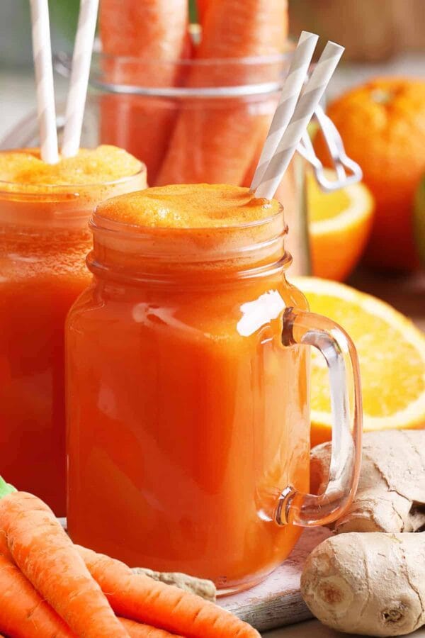 Cholesterol-Lowering Carrot Ginger smoothie in a glass, on my kitchen counter, surrounded by fresh fruit and vegetables.
