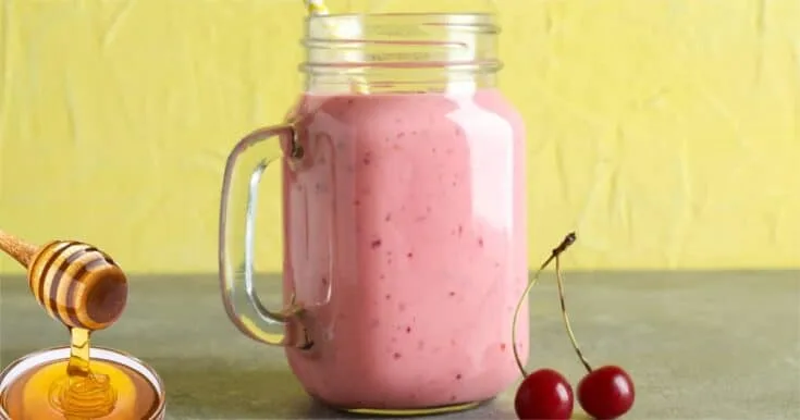 Cholesterol-Lowering Cherry Almond smoothie in a glass, on my kitchen counter, surrounded by fresh fruit and vegetables.