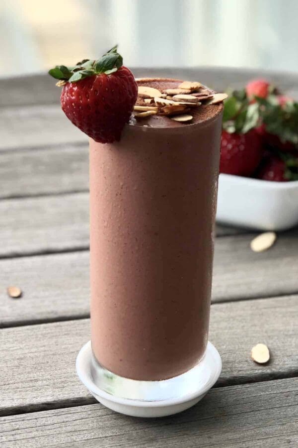 Cholesterol-Lowering Chocolate Strawberry smoothie in a glass, on my kitchen counter, surrounded by fresh fruit and vegetables.