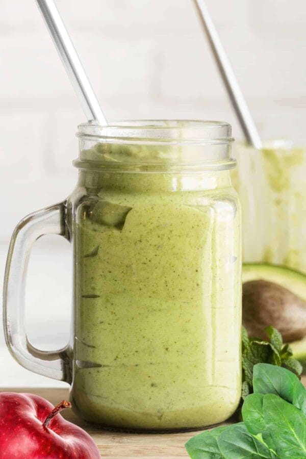 Cholesterol-Lowering Green Avocado smoothie in a glass, on my kitchen counter, surrounded by fresh fruit and vegetables.
