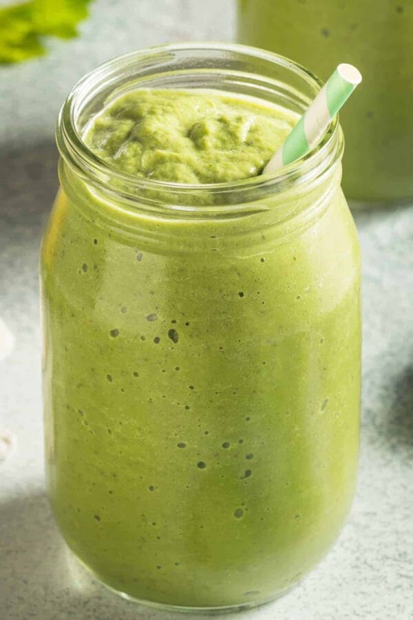 Cholesterol-Lowering Green Detox smoothie in a glass, on my kitchen counter, surrounded by fresh fruit and vegetables.