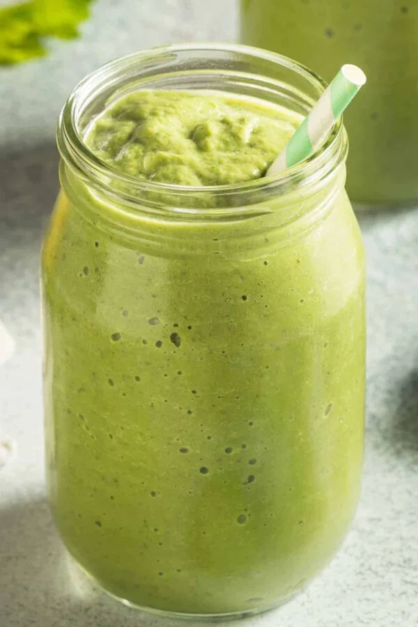 Cholesterol-Lowering Green Detox smoothie in a glass, on my kitchen counter, surrounded by fresh fruit and vegetables.