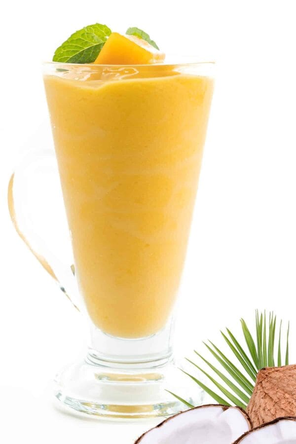 Cholesterol-Lowering Mango Coconut smoothie in a glass, on my kitchen counter, surrounded by fresh fruit and vegetables.