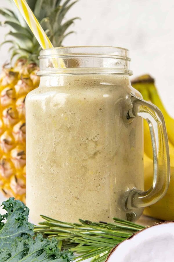Cholesterol-Lowering Pineapple Kale smoothie in a glass, on my kitchen counter, surrounded by fresh fruit and vegetables.