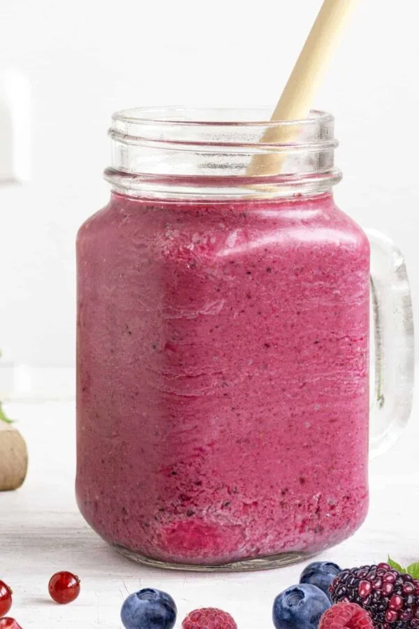 Cholesterol-Lowering Pomegranate Berry smoothie in a glass, on my kitchen counter, surrounded by fresh fruit and vegetables.