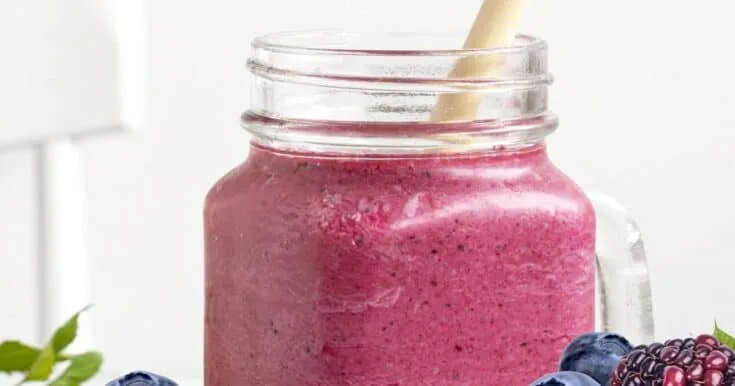 Cholesterol-Lowering Pomegranate Berry smoothie in a glass, on my kitchen counter, surrounded by fresh fruit and vegetables.