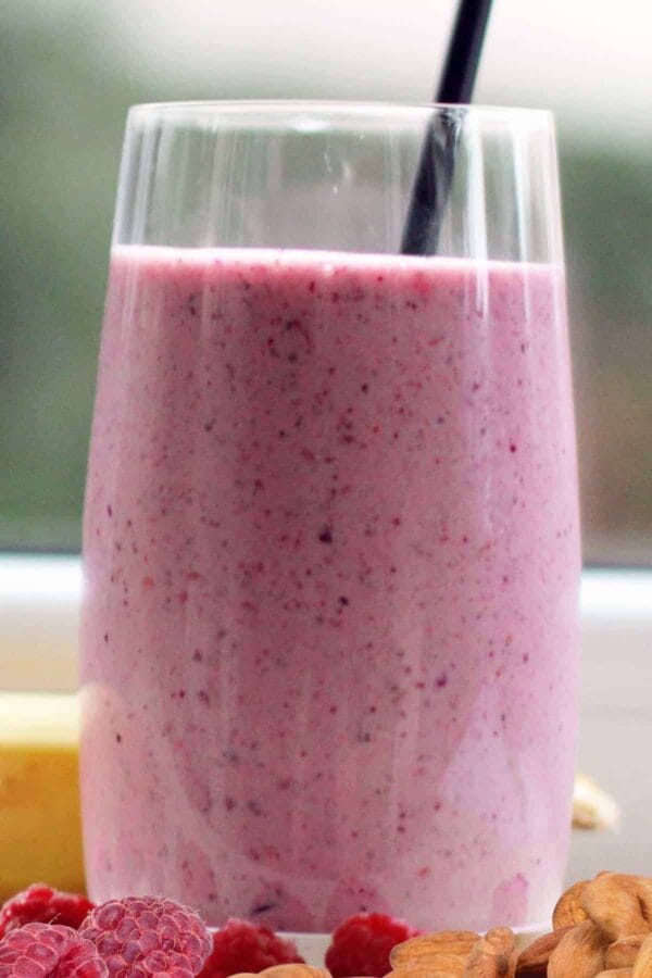 Cholesterol-Lowering Raspberry Almond smoothie in a glass, on my kitchen counter, surrounded by fresh fruit and vegetables.