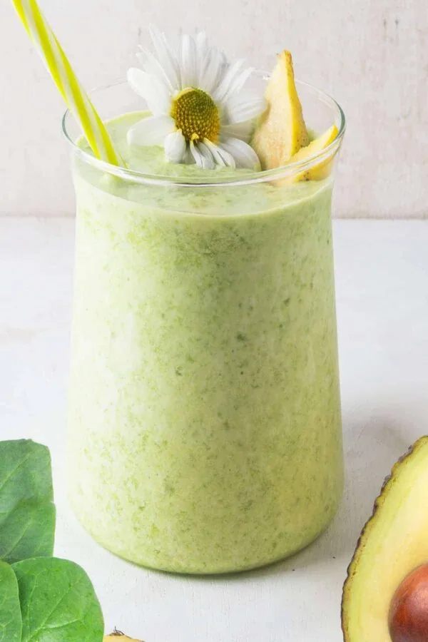 Cholesterol-Lowering Spinach Mango smoothie in a glass, on my kitchen counter, surrounded by fresh fruit and vegetables.