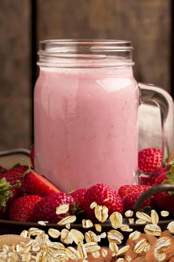 Cholesterol-Lowering Strawberry Oat smoothie in a glass, on my kitchen counter, surrounded by fresh fruit and vegetables.