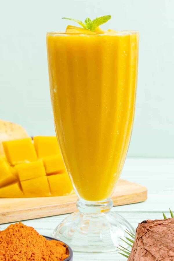 Cholesterol-Lowering Tropical Turmeric smoothie in a glass, on my kitchen counter, surrounded by fresh fruit and vegetables.