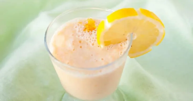 Detox Citrus And Green Tea smoothie in a glass, on my kitchen counter, surrounded by fresh fruit and vegetables.
