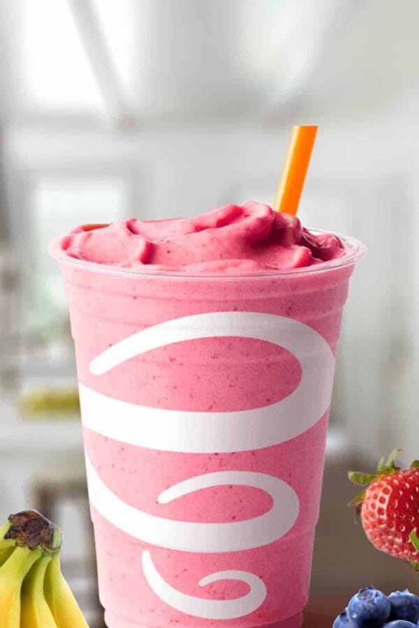 Jamba Juice Banana Berry smoothie in a glass, on my kitchen counter, surrounded by fresh bananas and berries.