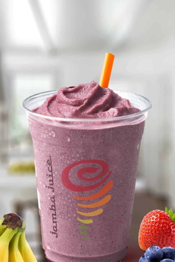 Jamba Juice Five Fruit Frenzy smoothie in a glass, on my kitchen counter, surrounded by bananas and fresh berries.