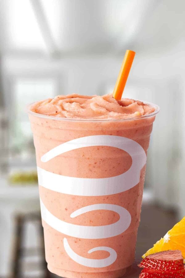 Jamba Juice Orange-A-Peel smoothie in a glass, on my kitchen counter, surrounded by fresh oranges and strawberries.
