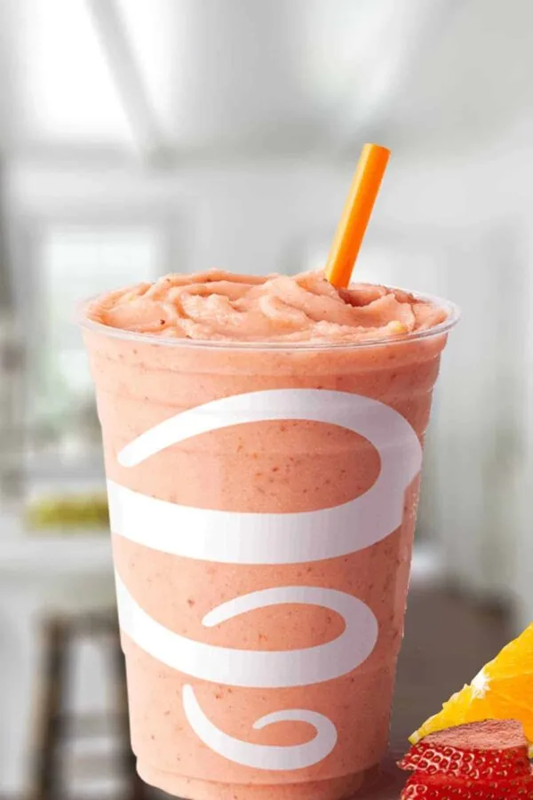 Jamba Juice Orange-A-Peel smoothie in a glass, on my kitchen counter, surrounded by fresh oranges and strawberries.
