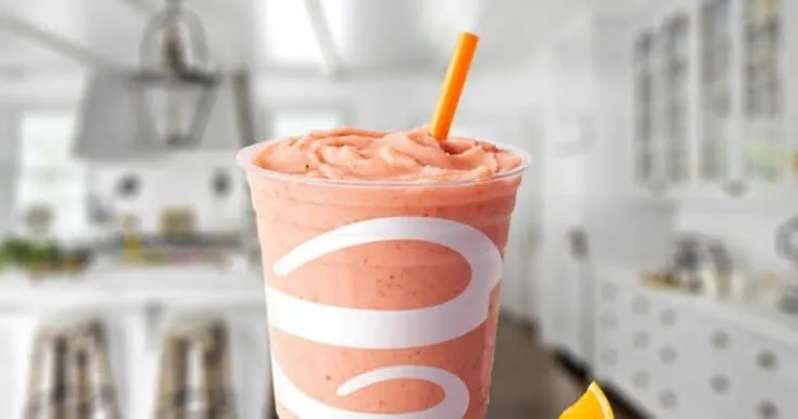 Jamba Juice Orange-A-Peel smoothie in a glass, on my kitchen counter, surrounded by fresh oranges and strawberries.