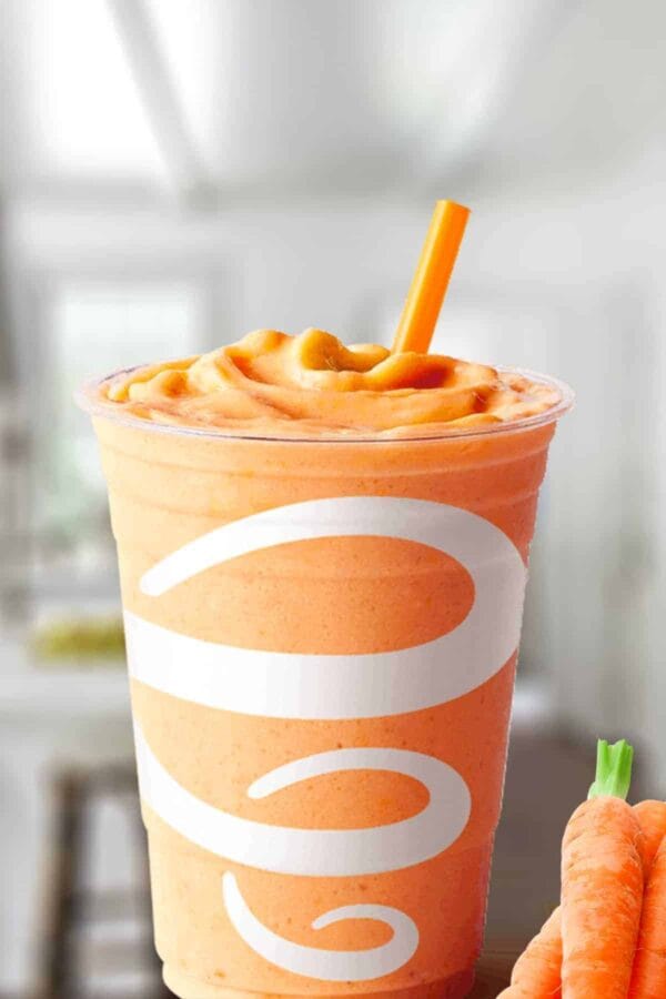 Jamba Juice Orange Carrot Karma smoothie in a glass, on my kitchen counter, surrounded by carrots.