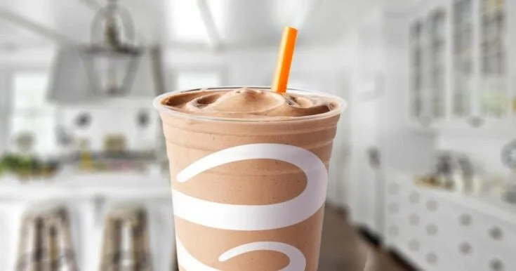 Jamba Juice Peanut Butter Moo'd smoothie in a glass, on my kitchen counter, flanked by a spoonful of peanut butter.