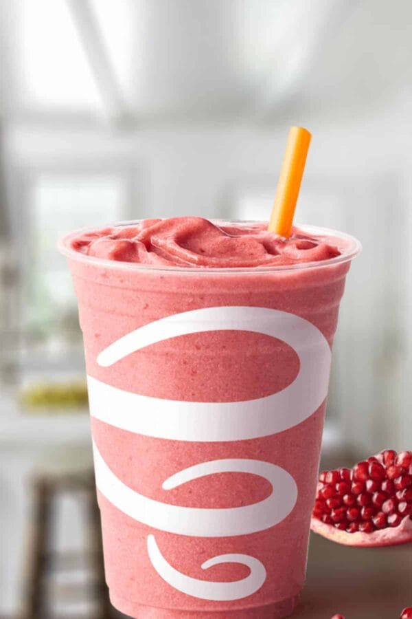 Jamba Juice Pomegranate Paradise smoothie in a glass, on my kitchen counter, surrounded by pomegranate seeds.
