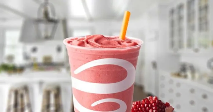 Jamba Juice Pomegranate Paradise smoothie in a glass, on my kitchen counter, surrounded by pomegranate seeds.