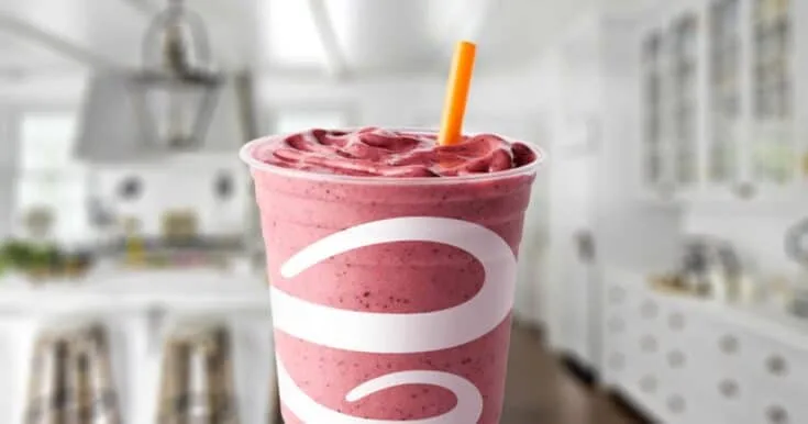 Jamba Juice Razzmatazz smoothie in a glass, on my kitchen counter, surrounded by fresh raspberries.