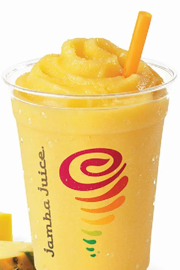 Jamba Juice Secret Menu Tropical Awakening smoothie in a glass, on my kitchen counter, surrounded by fresh fruit.