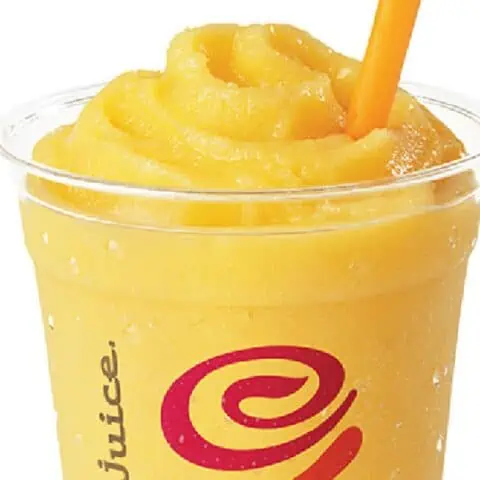 Jamba Juice Secret Menu Tropical Awakening smoothie in a glass, on my kitchen counter, surrounded by fresh fruit.