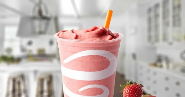 Jamba Juice Strawberry Whirl smoothie in a glass, on my kitchen counter, surrounded by fresh strawberries.