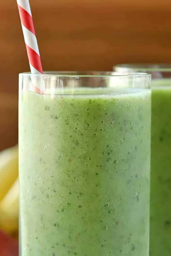 Liver Detox smoothie in a glass, on my kitchen counter, surrounded by fresh fruit and vegetables.