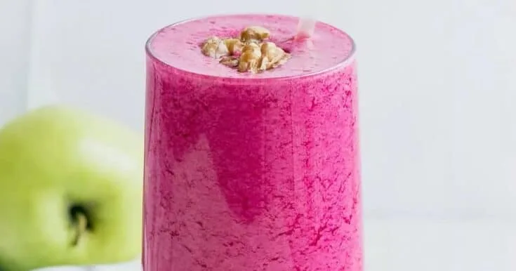 Simply Great Detox smoothie in a glass, on my kitchen counter, surrounded by fresh fruit and vegetables.