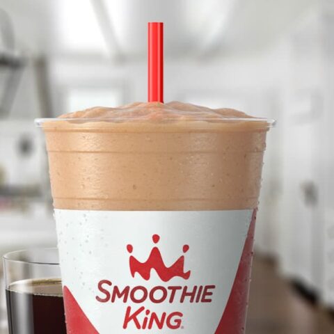 Smoothie King Espresso D-Lite Mocha moothie in a glass, on my kitchen counter, surrounded by coffee beans and chocolate.