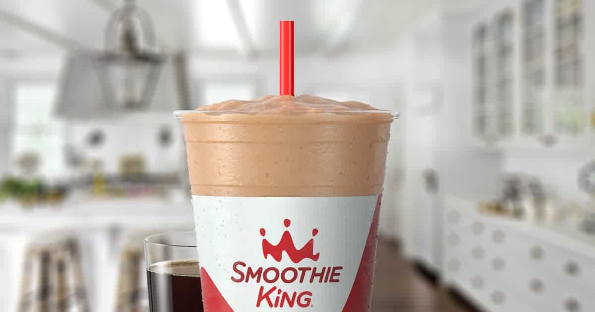 Smoothie King Espresso D-Lite Mocha moothie in a glass, on my kitchen counter, surrounded by coffee beans and chocolate.
