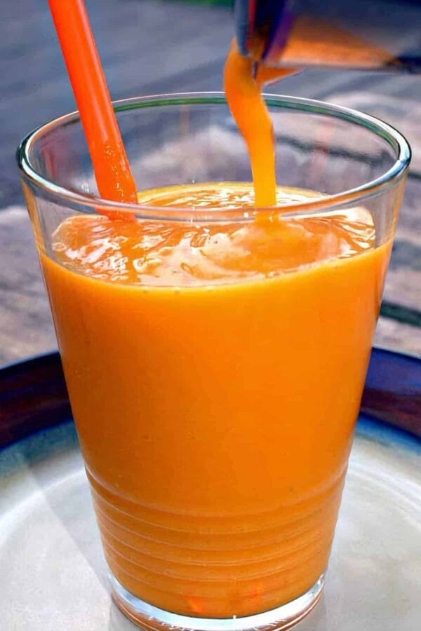 Tropical Papaya Detox smoothie in a glass, on my kitchen counter, surrounded by fresh fruit and vegetables.