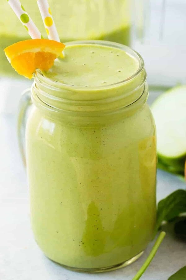 Tropical Turmeric Detox smoothie in a glass, on my kitchen counter, surrounded by fresh fruit and vegetables.