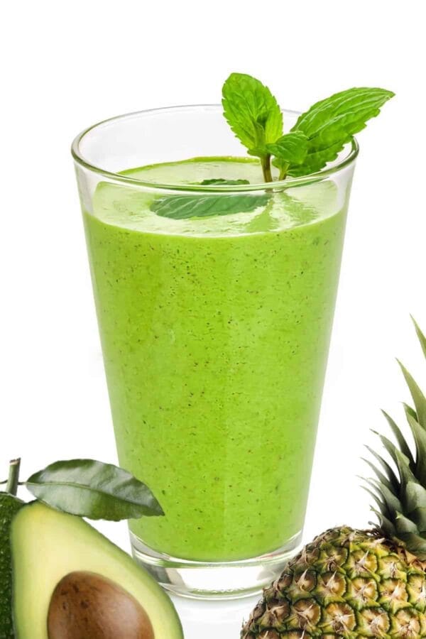 Vitamix Avocolada smoothie in a glass, on my kitchen counter, surrounded by fresh fruit and vegetables.