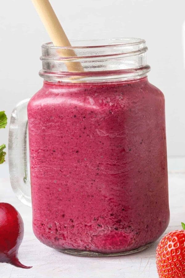 Vitamix Beet Strawberry Cranberry smoothie in a glass, on my kitchen counter, surrounded by fresh fruit and vegetables.