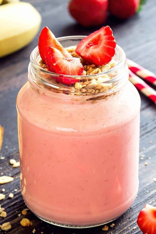 Vitamix Frozen Strawberry Banana Oat smoothie in a glass, on my kitchen counter, surrounded by fresh fruit and vegetables.