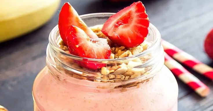 Vitamix Frozen Strawberry Banana Oat smoothie in a glass, on my kitchen counter, surrounded by fresh fruit and vegetables.