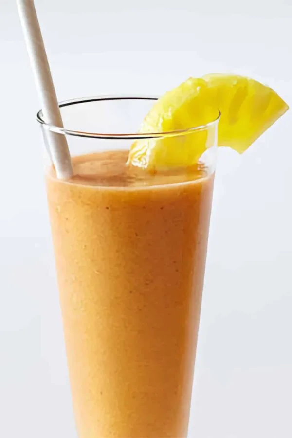 Vitamix Fruit Salad smoothie in a glass, on my kitchen counter, surrounded by fresh fruit and vegetables.