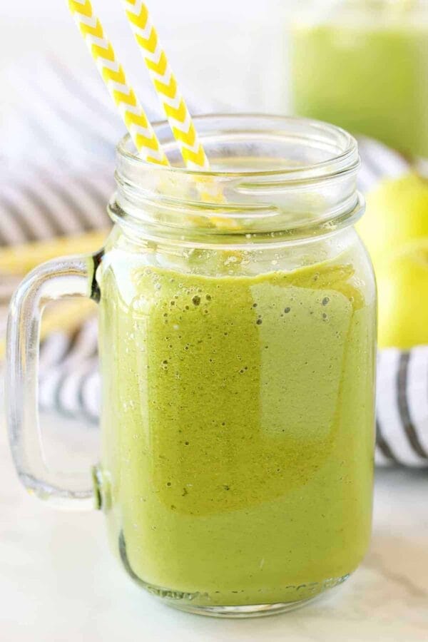Vitamix Good Morning Green smoothie in a glass, on my kitchen counter, surrounded by fresh fruit and vegetables.