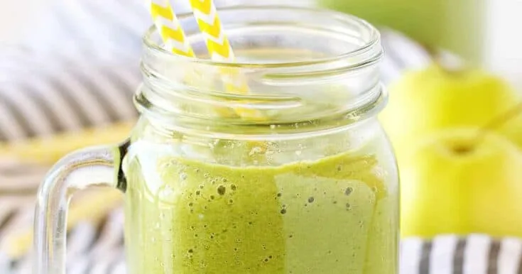Vitamix Good Morning Green smoothie in a glass, on my kitchen counter, surrounded by fresh fruit and vegetables.