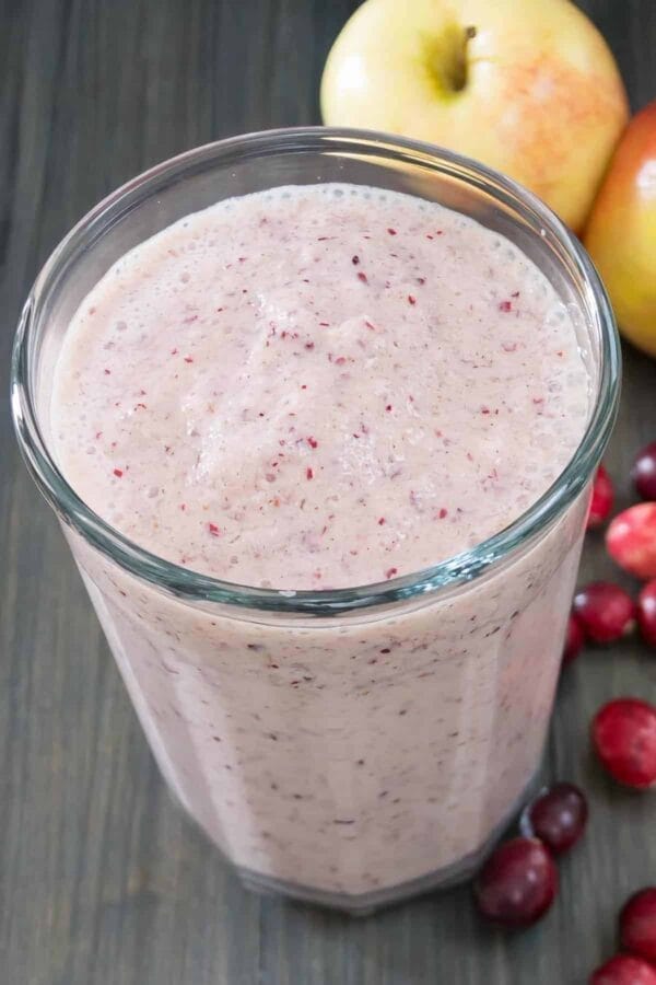 Vitamix Holiday Fruit smoothie in a glass, on my kitchen counter, surrounded by fresh fruit and vegetables.