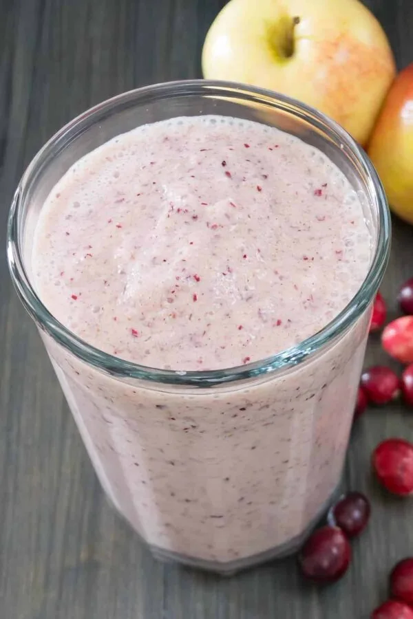 Vitamix Holiday Fruit smoothie in a glass, on my kitchen counter, surrounded by fresh fruit and vegetables.