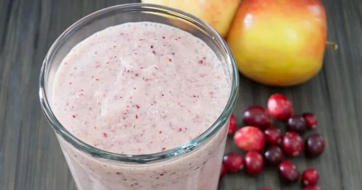 Vitamix Holiday Fruit smoothie in a glass, on my kitchen counter, surrounded by fresh fruit and vegetables.