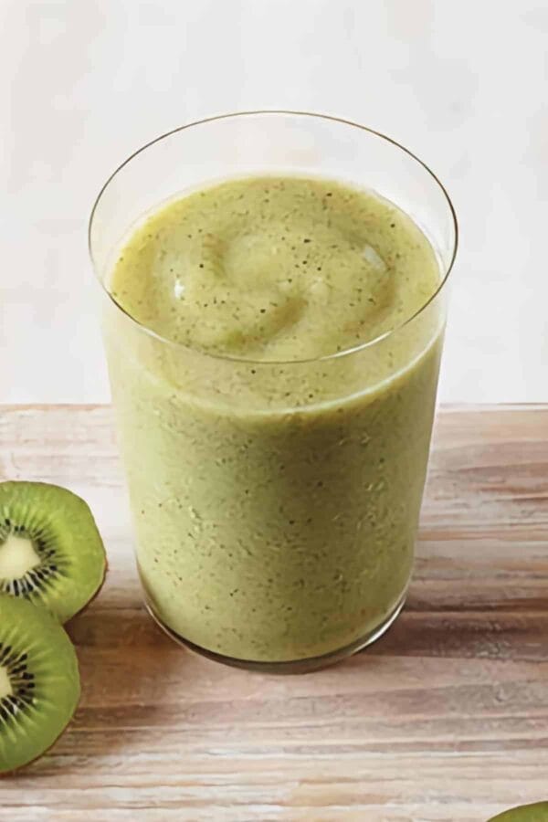 Vitamix Key Lime Kiwi smoothie in a glass, on my kitchen counter, surrounded by fresh fruit and vegetables.