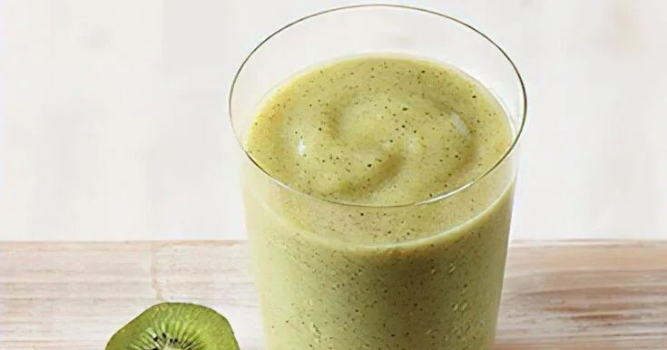 Vitamix Key Lime Kiwi smoothie in a glass, on my kitchen counter, surrounded by fresh fruit and vegetables.