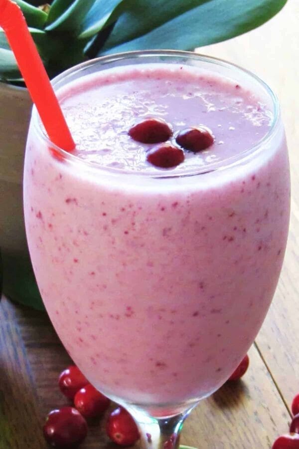 Vitamix Passionately Pink smoothie in a glass, on my kitchen counter, surrounded by fresh fruit and vegetables.